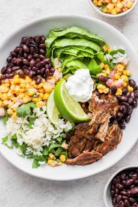 Delicious, healthy Slow Cooker Carnitas Burrito Bowls made with slow-cooked carnitas, Mexican street corn salad, and cilantro lime rice!