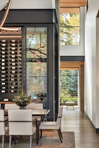 Within reach of a bespoke live-edge walnut-and-brass dining table, a glass temperature-controlled wine room showcases the homeowners’ collection. The ombre silk rug is Rosemary Hallgarten. Overhead hangs Ovuud’s multi-arm Woven pendant.