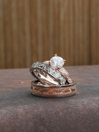 You're a couple with a classic, laid-back, vintage style- and you need the rings to match that vibe. This gorgeous set is just for you, with an amazing vintage Western look.  All with coordinating metals and hand-engraving, this Western wedding ring trio features: The rose gold engagement ring: Made out of 10K rose gold, this beautiful 3.5mm ring has hand-engraved details that swirl continuously around the ring. A beautiful round 1.25 ct moissanite is in the center of the ring. This ring is time