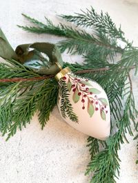 FREE SHIPPING! This is a one-of-a-kind, ceramic, hand-painted Christmas ornament. Beautifully crafted, this heirloom piece of art will hopefully be passed along for years to come. Includes a gorgeous gold cap and hangs from a raw-edged sage green cotton ribbon. Set on a soft beige background, cascading sprigs of leaves and berries and pine takes center stage with organic shades of green, burgundy and chestnut.  Each ornament is sealed in a matte finish, for protection. This teardrop shaped ornam