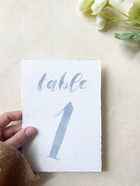 "What size are these digitally printed handmade paper table numbers? 5\" x 7\" sold in single-sided sets of 1-10 or 1-20. These are not double sided. These handmade paper table cards will fit right in with your wedding decor. Digitally printed with a classic watercolor font, your guests will find their seats with ease. This style is perfect for laid back or rustic weddings or bridal showers.  The photo is of a handmade paper place card. Gold frame NOT included.  All products are shipped in secur