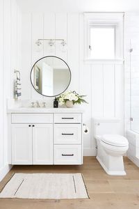 Cottage bathroom boasting a charming look features a round black mirror on a vertical tongue and groove wall above a white single washstand.