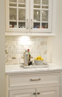 Beautiful kitchen with white cabinetry pairing with nickel hardware alongside Calcutta Gold Marble countertops with a Beveled Calcutta Gold Marble subway tiled backsplash below glass front cabinetry.