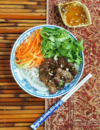 Aerial view of Bún Thịt Nướng (Vietnamese Grilled Pork with Rice Noodles) next to white and blue chopsticks and dipping sauce in a leaf-shaped bowl.