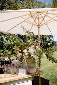 An open air cocktail bar on a big lawn makes for a beautiful garden party setting. Keeping things cool with a sun umbrella over the gorgeous florals! #gardenparty #wedding #outdoorwedding #weddingreception #luxuryweddingplanner