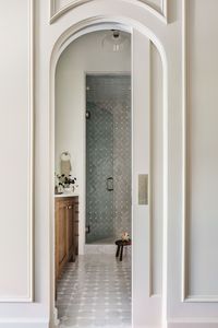 Primary bathroom suite with arched doorways, finish work, tile floors and tiled shower, and wood vanity.