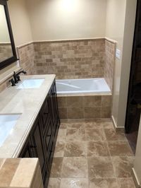 This Best Builders Group bathroom remodeling project features a black bathroom vanity, double bathroom sinks, a large black mirror, gorgeous tan bathroom tiles, and a large soaking bathtub. #bathroomremodel #bathroommakeover #bathroominspiration 