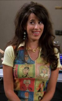 Maggie Wheeler as Janice from 'Friends' (1994) S3 E4 'The One With The Metaphorical Tunnel' (1996) wearing a short sleeved, collared top decorated with colorful artistic panels of faces.