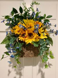 "Welcome your guests with this beautiful, bright and sunny door basket wreath.  This medium sized basket wreath is a unique alternative to the traditional door wreath.  This nicely woven wall pocket/basket has a handle for hanging and is filled with a variety of high quality and realistic sunflowers, blue wild daisies, variegated ivy, ruscus, seeded eucalyptus and round eucalyptus.  A one of a kind a simply beautiful decoration for any area in your home or give as a great gift and watch them smi