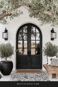 Welcome guests in style with this modern farmhouse entrance inspired by Marrakesh! 🖤✨ Featuring tall black arched doors, Moroccan tile accents, and rustic lanterns, this monochrome entrance blends elegance with farmhouse charm. Surrounded by olive trees, it's the perfect first impression for your home! #FarmhouseEntrance #MoroccanInspo #MonochromeDesign #RusticFarmhouse #FrontDoorGoals