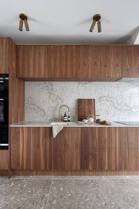 Warm Wood Cabinets with Marble Backsplash and Brass Lighting Fixtures Another mid-century kitchen design with warm wood cabinetry crowned with many other Mid-century-inspired fixtures to bring cohesion to the space!