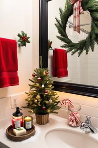 Add holiday cheer to your bathroom with these easy Christmas decor ideas! A festive red towel on the rack pairs perfectly with a wreath on the mirror, while a candle with a pine scent and holiday-themed soaps sit on the countertop. A mini Christmas tree in the corner, with tiny lights and ornaments, brings the seasonal spirit to the space. Sprinkle a bit of faux snow around the tree for a winter touch that’s both simple and festive.