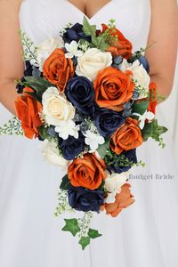 This cascading brides’ bouquet is the perfect option if you have chosen burnt orange or navy blue as one of the accent colors for your wedding. A lovely array of roses in burnt orange, navy blue and ivory roses with white stephanotis, greenery and blue berries that are center-stage in this stunning arrangement. Lush foliage in dusty green completes this romantic and beautiful design, in addition to white stephanotis. As always, this bouquet has been wired by hand and designed by our in-house flo