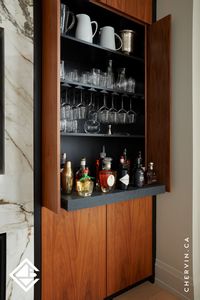 These stunning walnut pocket doors with touch and release functionality conceal a hidden gem—a cocktail bar! Behind these doors, you'll find shelving, a wine stem rack, and a stone roll-out shelf for easy access to items at the back. #PocketDoor #PocketDoors #CocktailBar #BarCabinet