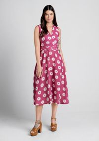 In classic 1960’s retro fashion, this cheerful sleeveless midi dress from Timeless London is adorned throughout in a playful and swirly white daisy print. Made from a magenta pink, lightweight woven fabric, this floral dress boasts a surplice neckline, a high-rise waist cinched with a matching and removable belt, and a flowy mid-length skirt with handy side pockets.