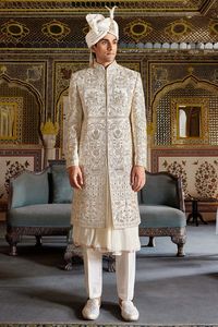 The luxurious raw silk in this cream-colored sherwani is enhanced with embroidery, resham, beads, stone, zardosi , sequins work. Designed in peshwai style, it offers both sophistication and comfort, while the matching bottom add the perfect finishing touch for the groom.