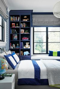 Blue and gray kids's room features blue built in shelves with a window seat and a gray linen bed with blue and white bedding, blue geometric wallpaper and a globe on a white nightstand lit by a white round globe light.