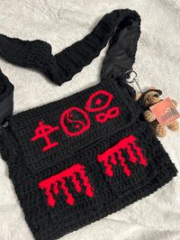 Crocheted messenger bag with Bad Omens TDOPOM symbols stitched on the front! Also has 2 little pockets in the front with a dripping blood design. This bag is  lined with cotton fabric to avoid stretching, and also includes 2 magnetic enclosures. Added bonus- a keychain of a teddy bear wearing headphones and holding a mini TDOPM album!