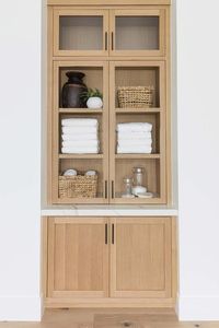 Built in tan wooden bath linen cabinet boasts glass doors.