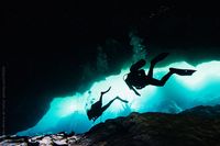 Silhouette of scuba divers diving in a dark underwater cave by Alejandro Moreno de Carlos for Stocksy United