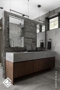 This custom walnut vanity with kerf-line accents and a sleek concrete countertop creates a stunning focal point in this modern industrial main bathroom. A bold stone wall divider completes the design. #BathroomVanity #BathroomVanityIdeas #BathroomVanityGoals #WalnutVanity #ConcreteCountertop