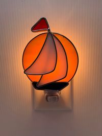 Orange Sunset with Sailboat Overlay in White Stained Glass Nightlight, Small Blue Boat and Tiny Red Flag, with Free Gift Box. Beautiful soft glow at night. Perfect Hand Crafted Holiday Gift Created in Suncook, NH using traditional, authentic stained glass method. The Process: Design and trace the template, score each sheet of glass, then snap into rough shapes, grind to smooth the edges, wrap in stretched lead came and solder at all points and the pieces are layered, soldered together to create