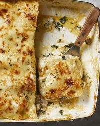 An overhead view of slice of white lasagna being lifted out of a baking dish on a white marble background