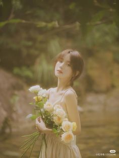 a woman holding flowers in her hands near water