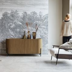 a woman walking past a wall with a painting on it's sideboard next to a couch