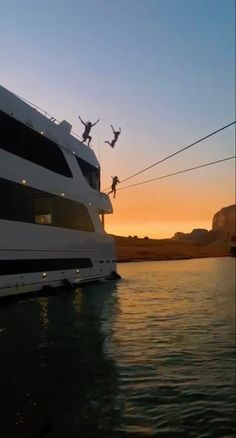 two people are jumping off the side of a boat into the water at sunset or dawn