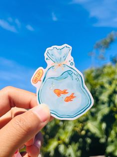 a hand holding up a sticker with an image of a fish in a bag