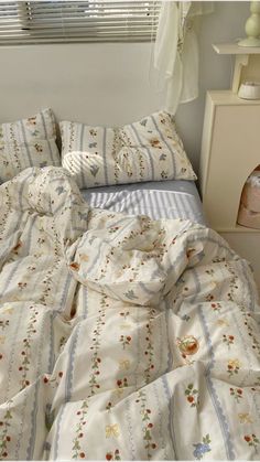 an unmade bed with white and blue comforter in a bedroom next to a window