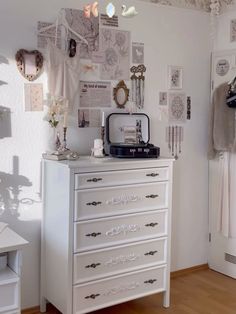 a white dresser sitting in a bedroom next to a wall covered with pictures and jewelry