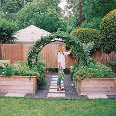 a woman standing in the middle of a garden with potted plants on either side