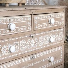 an old dresser painted with white paint and flowers on the drawers is sitting next to a wicker basket