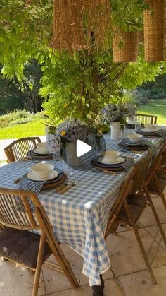 a table set with plates and place settings under a tree in the backyard, surrounded by greenery