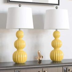 two yellow lamps sitting on top of a dresser next to a mirror and lamp shade