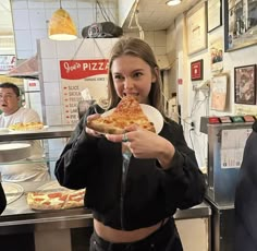 a woman holding a slice of pizza in front of her face while standing next to a counter