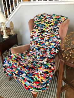 a chair covered in multicolored crocheted fabric next to a wooden table