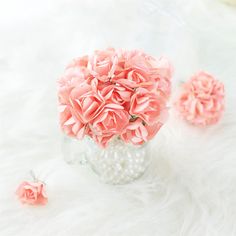 pink flowers are in a clear glass vase on a white furnishing with pearls