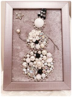 a snowman made out of beads and other items in a frame on a table