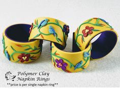 three yellow and blue flower decorated bangles on a white tableclothed surface, one with flowers painted on it