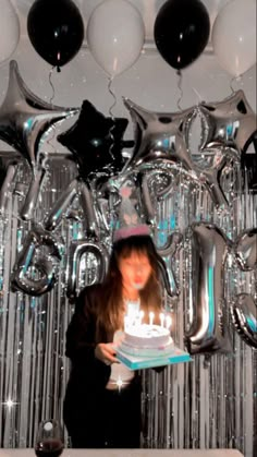 a woman holding a birthday cake in front of balloons