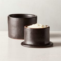 two black pots with whipped cream in them sitting on a table next to each other