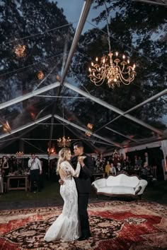 a bride and groom dance under a tent at their wedding reception with chandeliers hanging from the ceiling