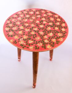 a red table with flowers painted on the top and wooden legs, against a white background