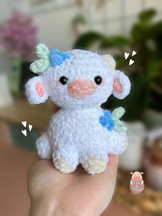 a small white stuffed animal with blue flowers on it's head is held in a hand