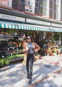 a woman is walking down the sidewalk in front of an antique store with flowers and plants