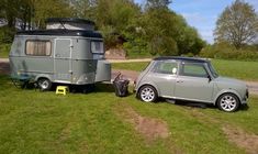 a small car parked next to a trailer in the grass with a camper behind it