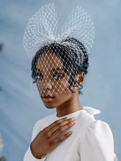 a woman wearing a birdcage veil with her hands on her chest and looking off to the side